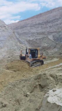 Buldozer kumlu taş ocağı yamaçlarını tarıyor, dozer takip ediyor büyük bıçağı gevşek kumda itiyor, kıvrımlı taşıma yolu oluşturuyor.