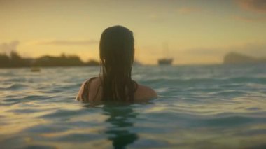 Suda altın gün batımı okyanus kadını, sırtını döndü, örgülü saçlar, nazik dalgalar, ufukta demirli yelkenliler, sıcak