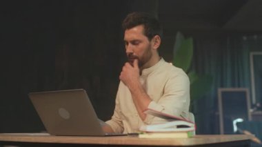 Beyaz adam belgeleri ve dizüstü bilgisayarları inceliyor, renkli sekmeleri olan dizinler, elinde kalem, düşünceli ifade, sıcak