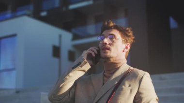 Basamaklarda konuşan beyaz adam telefon, yün ceket ve deri çanta, şirket lobisinin dışındaki şehir merdivenleri, akşam parıltısı.,