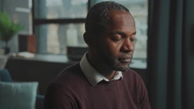 Siyahi adam pencereye yaslanıyor, yaratıcı engellerle güreşiyor, sürekli yakın plan portre, sessiz tonlar, düşünceli.