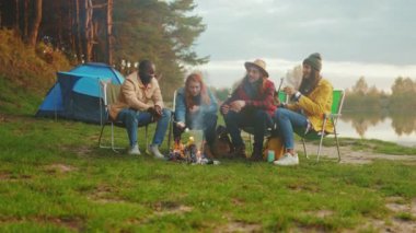 Grup arkadaşları göl kenarında kamp yapıyor, küçük kamp ateşinin etrafında gitar tıngırdatıyorlar, gülüyor ve renkli hikayeler paylaşıyorlar.