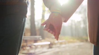 Parkta el ele tutuşan çiftler, birbirine kenetlenmiş ellerde gökkuşağı bileziği ve rahat ceketler, yumuşak güneş ışığı...