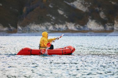 Sürünün içinde yüz. Packraft, tek kişilik hafif sal. Sefer ya da macera yarışı için kullanılan. Bir gölde, şişme bir teknede.