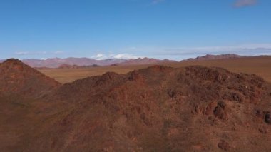 Mavi gökyüzü ve dağlar. İnsansız hava aracı dağın üzerinde uçuyor. Vahşi doğadaki dağ manzarası.
