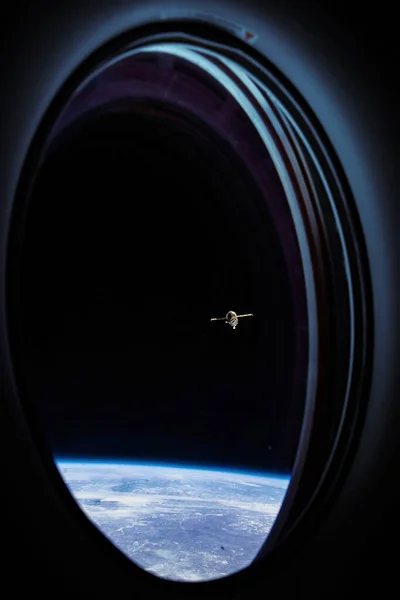 View on ISS Progress 76 resupply ship looks out from a passenger window on the SpaceX Crew Dragon Resilience. Docking maneuver near the Space Station. Elements of image furnished by NASA.