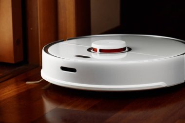 Ahşap zeminde akıllı robot elektrikli süpürge. Robot elektrikli süpürge daireyi belli bir zamanda otomatik olarak temizliyor. Akıllı ev