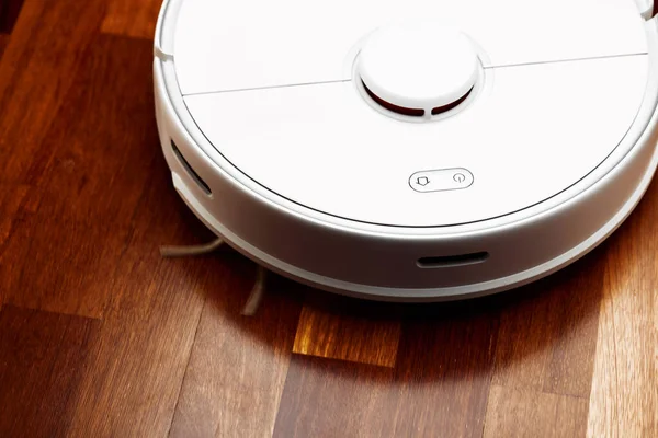 Smart Robot Vacuum Cleaner on wood floor. Robot vacuum cleaner performs automatic cleaning of the apartment at a certain time. Smart home