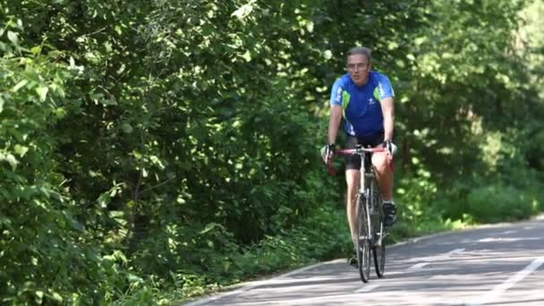 Velho está pedalando uma bicicleta no parque - curtindo esporte ou hobby vivendo saudável. Andar de bicicleta no parque, manter-se em forma na idade adulta. Vídeo 4K slow motion de 120 fps. 28.08.2021, Região de Moscovo — Vídeo de Stock