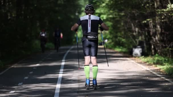 Allenare un atleta sui pattini a rotelle. Giro in biathlon sugli sci a rotelle con racchette da sci. Allenamento tra le stagioni sugli sci a rotelle nel parco. Video al rallentatore 120 fps. 28.08.2021, Regione di Mosca — Video Stock