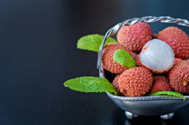 Taze organik liçi meyvesi metal kasede bacakları siyah arka planda, üst manzara