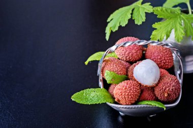 Taze organik liçi meyvesi metal kasede bacakları siyah arka planda, üst manzara