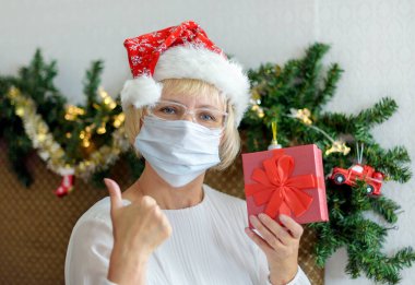 Gülümseyen orta yaşlı, tıbbi maskeli ve Noel Baba şapkalı bir kadın. Noel için uzaktan tebrik ederim. Salgın