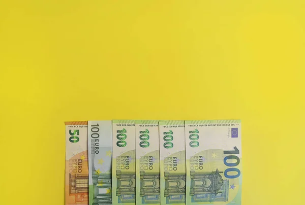 Banknotes of 100 Euro. European currency banknotes isolated on a yellow background. Close-up view from above. The concept of the European Union\'s economic crisis