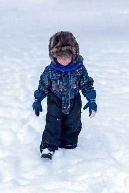 Kar yağarken dışarıda oynayan kürk şapkalı komik çocuk. Soğuk karlı günlerde çocuklarla aktif dinlenme. Düşünceli çocuk.