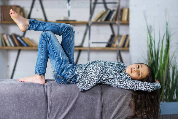 Uzun saçlı, rahat bir kanepede sırtüstü uzanmış, elleri başının arkasında rahatlamış genç bir kız.