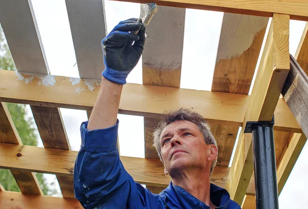 労働者は彼の家の木製の屋根を塗装し 家は建設中です — ストック写真