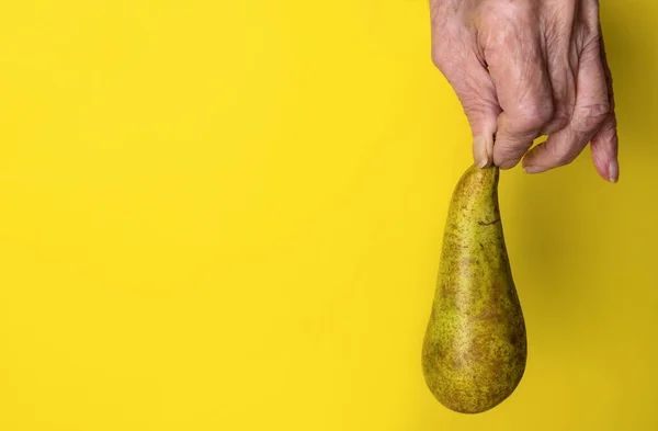 一位老年妇女的手把梨子放在黄色的背景上 — 图库照片