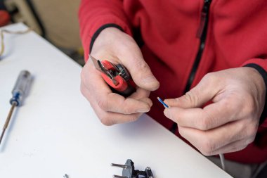 Ev hobisi. Beyaz bir arka planda elektrik kablosu üzerinde çalışan, elinde inşaat bıçağı olan beyaz bir adamın ellerine yakın plan.