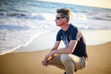 Güneşli giysiler içinde yetişkin bir adam plajda yaz tatilinin tadını çıkarıyor.