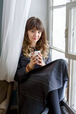 Elbiseli genç esmer kadın hayal kurarak pencerede oturuyor..