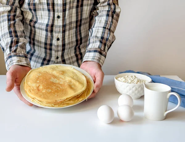 A lot of pancakes are stacked on a white plate. Thin pancakes with a crispy crust. Pancake day. Pancakes for breakfast and carnival. Food background.