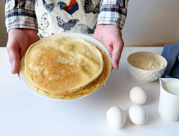 A lot of pancakes are stacked on a white plate. Thin pancakes with a crispy crust. Pancake day. Pancakes for breakfast and carnival. Food background.