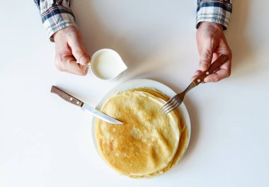 Çatal ve bıçakla erkek eli. Beyaz bir tabakta bir sürü krep var. Kıtır kıtır olmuş ince krepler. Krep günü. Kahvaltı ve karnaval için gözleme. Gıda arkaplanı.