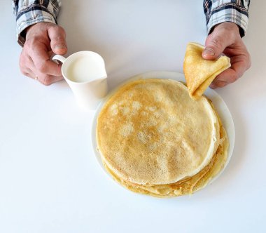 Erkeklerin elinde süt ve krep var. Beyaz bir tabakta bir sürü krep var. Kıtır kıtır olmuş ince krepler. Krep günü. Gıda arkaplanı.