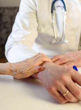 Yaşlı bir hasta elini klinikteki yaşlı bir doktorun koluna koydu..