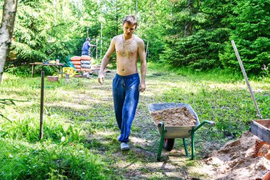 İnşaat işçisi kumlu bir el arabası kullanıyor. Bir evin inşaatında kullanılan beton karıştırma makinesi malzemeleri.