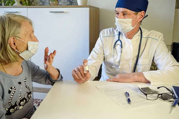 Caring doctor helps a negative elderly grandmother of 85 years-a patient at home or in the hospital. The concept of health care for the elderly. Denial of vaccination
