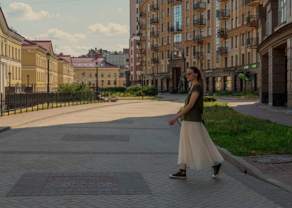一个穿着长裙 提着袋子穿过街道的年轻漂亮的女人 望着别处 夏天在圣彼得堡散步的女孩 — 图库照片