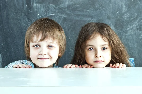 Boy and girl hiding behind a table near the school board — Stock Photo, Image