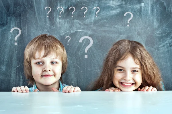Boy and girl hiding behind a table near the school board — Stock Photo, Image