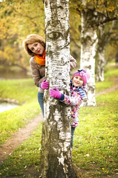 Dívka a matka se schovávají za stromem v podzimním parku — Stock fotografie