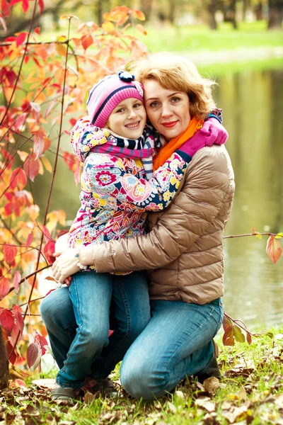 Fille et mère se cachent derrière un arbre dans le parc d'automne — Photo