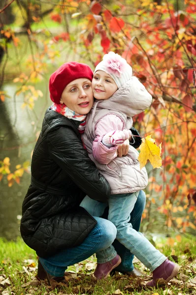 Dívka a matka se schovávají za stromem v podzimním parku — Stock fotografie