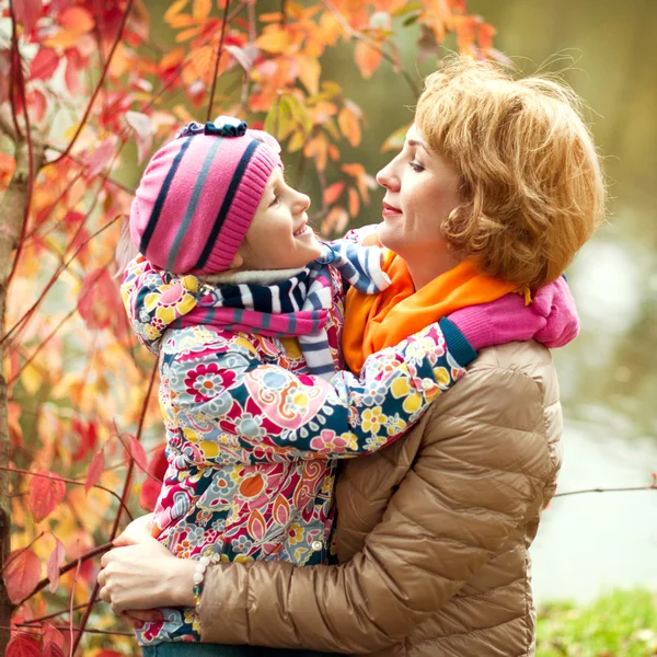 Dívka a matka se schovávají za stromem v podzimním parku — Stock fotografie