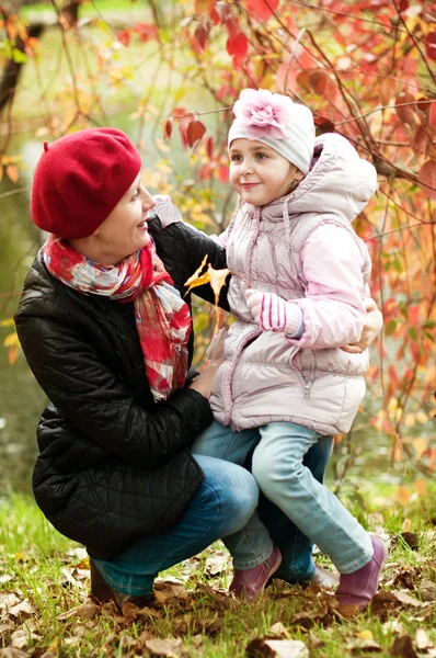 Dívka a matka se schovávají za stromem v podzimním parku — Stock fotografie