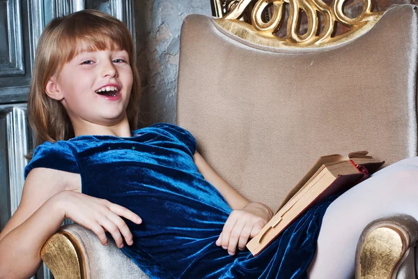 Chica feliz sentada en una silla con un libro — Foto de Stock