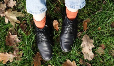 Yeşil çimlerin üzerinde siyah çizmeli kadın bacakları ve parkta düşen sarı sonbahar yaprakları. Sonbahar konsepti. Sonbahar yeşilliklerinde kadın ayakkabıları.