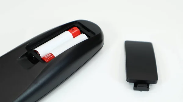 Zwarte TV afstandsbediening met AAA alkaline batterijen in rood en wit op een witte achtergrond. Batterijvervanging, reserveonderdelen. Afstandsbediening batterijvak close-up. — Stockfoto