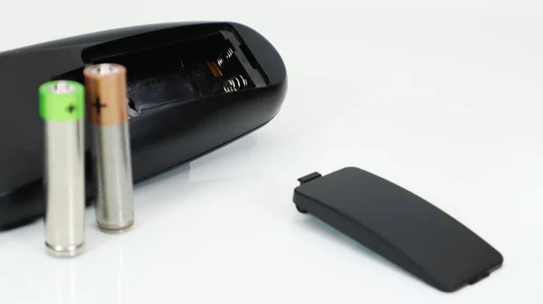 Zwarte TV afstandsbediening met AAA alkaline batterijen op een witte achtergrond. Batterijvervanging, reserveonderdelen. Sluiten van een lege batterijruimte van de afstandsbediening. — Stockfoto