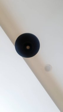 Tavandan sarkan siyah yuvarlak avize ya da beyaz lamba. Ampulün alt görüntüsü. Tavanda mimari dekorasyon, avizenin etrafında asılı. Minimalizm