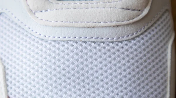 White color mesh fabric on a part of sports shoes. Running shoe net. Sportswear textured lattice. Textile texture background. Detail of a white sneaker in fabric with laces. Fragment of sports shoes