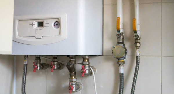 A gas double-circuit boiler is installed in the apartment. Autonomous heating boiler with a control panel, buttons, a display with temperature readings and red valves on pipes in a home kitchen