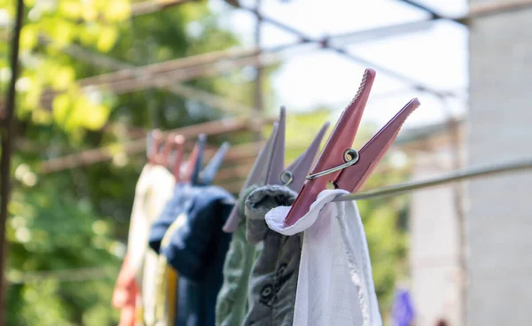 プラスチック製の服ピンはロープの上の行にかかっています 日当たりの良い庭のぼやけた背景に 屋外でロープ 通りの服を着て 服ピン — ストック写真