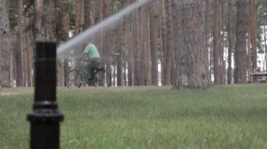 Yeşil bir parkta çim sulama sistemi çalışıyor. Sıcak havada çimenleri suyla ıslatıyorlar. Otomatik fıskiye. Otomatik sulama fıskiyesi başı çimleri suluyor. Akıllı bahçe.