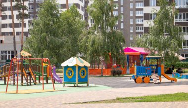 Bahçede, parkın içinde insanların olmadığı renkli, modern bir oyun bahçesi. Çocuklar için açık hava atlıkarıncasını salla. Yeşil ağaçlar ve yeni evlerle çevrili bir parkta oyun parkı. Çocuk egzersizi